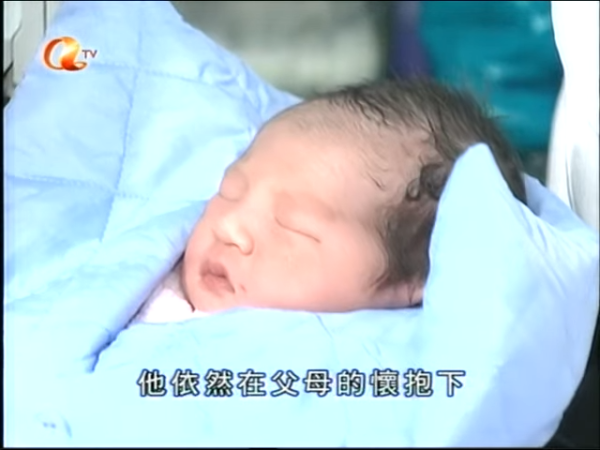 新聞主持形容BB「眼矇朦」，即使被大批傳媒包圍，仍在父母懷中睡得香甜。（網上截圖）