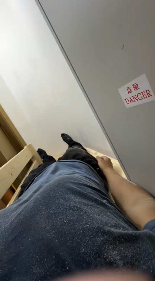 安裝員工示範躺上床，可見雙腳及身體幾乎頂住牆身，與電箱近距離相對。（截圖：Facebook）