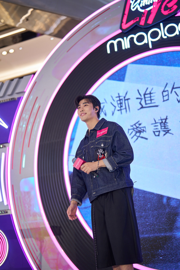 歌手Phoebus吴启洋身穿深色牛仔外套与宽裤,手持麦克风在舞台上微笑看着观众演唱。