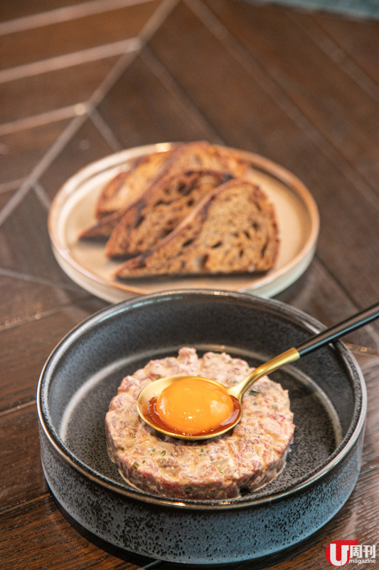  生牛肉他他（任食）以蛋黃醬、青瓜、乾葱碎等連同牛肉混製而成，食前再戥穿蛋汁，香滑細膩，層次豐富。